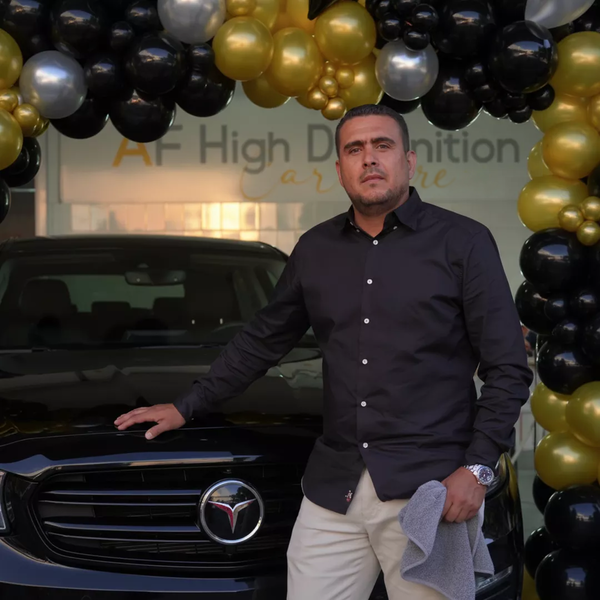 Fundador de AF High Definition frente al taller con arco dorado y SUV negro